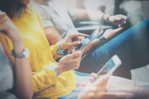 Group of young hipsters sitting on sofa holding en hands and using digital tablet, smartphone.Coworking team concept.Horizontal, blurred background