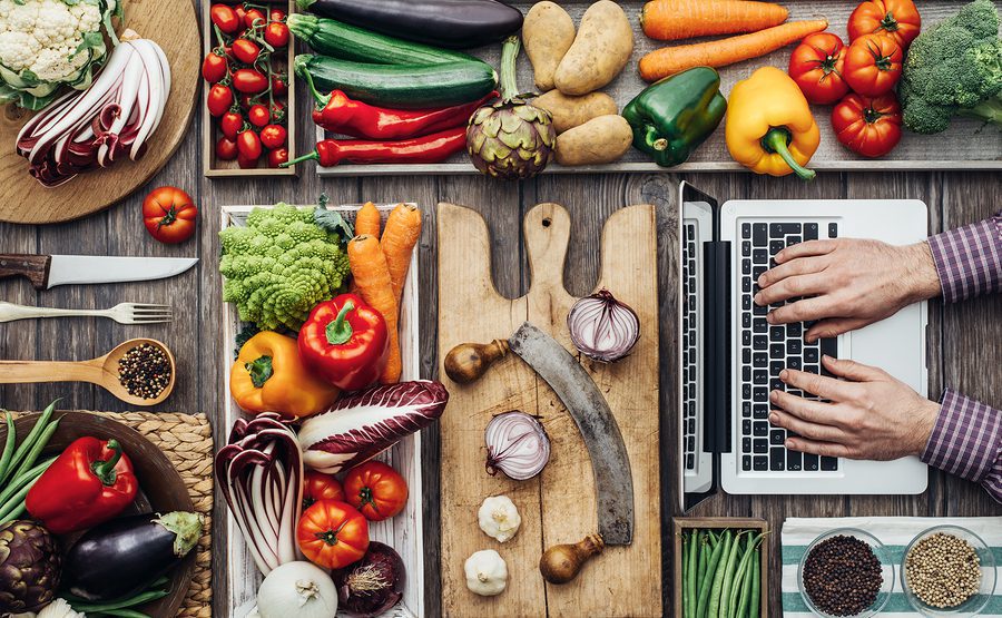 Freshly harvested vegetables cooking utensils and a laptop on a rustic kitchen worktop a man is searching recipes online