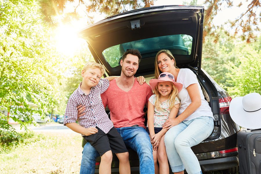 Happy family with children is sitting at the car in the summer