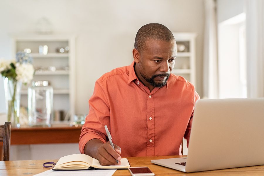 a guy working with his laptop and taking notes